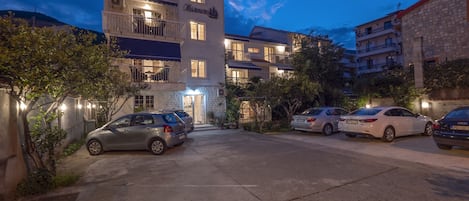 A multi-story hotel with a sign reading "Maunero" on the facade. There are several cars parked in the driveway.