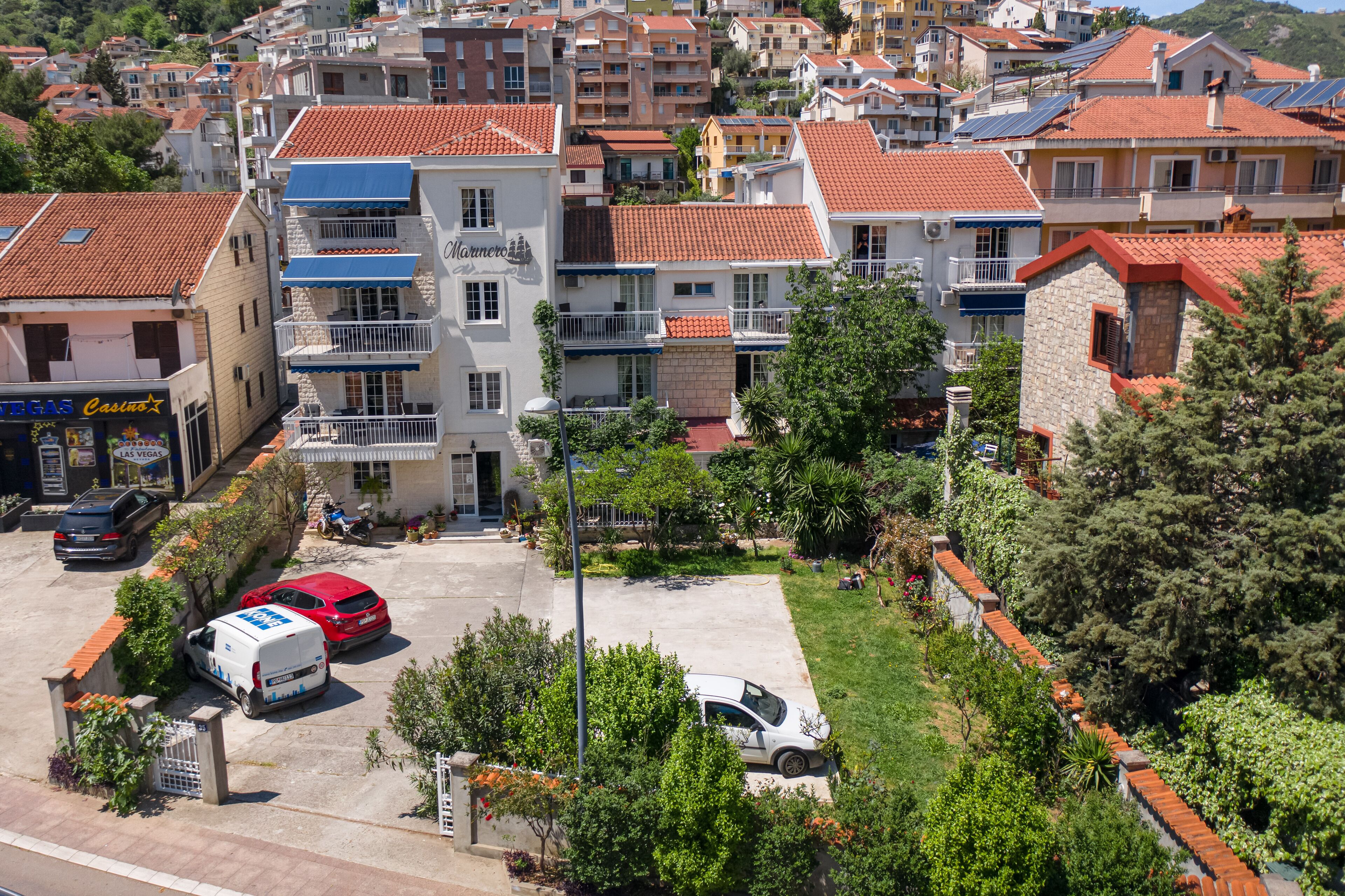 A multi-story building with balconies, a parking area, and surrounding greenery.