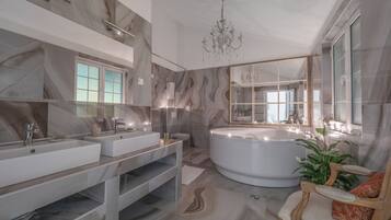 Un baño moderno con dos lavamanos, una bañera grande, una araña y un espejo con marco decorativo.