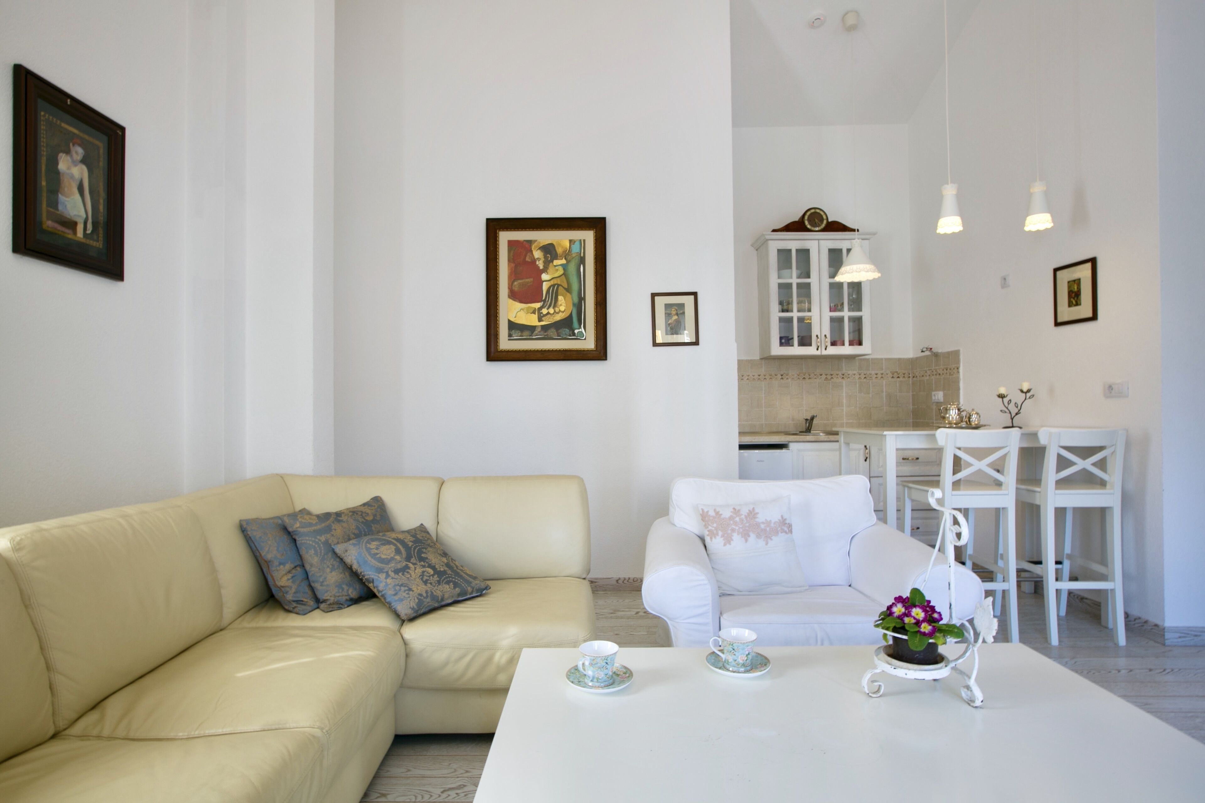 A living room with a beige sofa, a white armchair, and a coffee table with two cups and a flower vase.