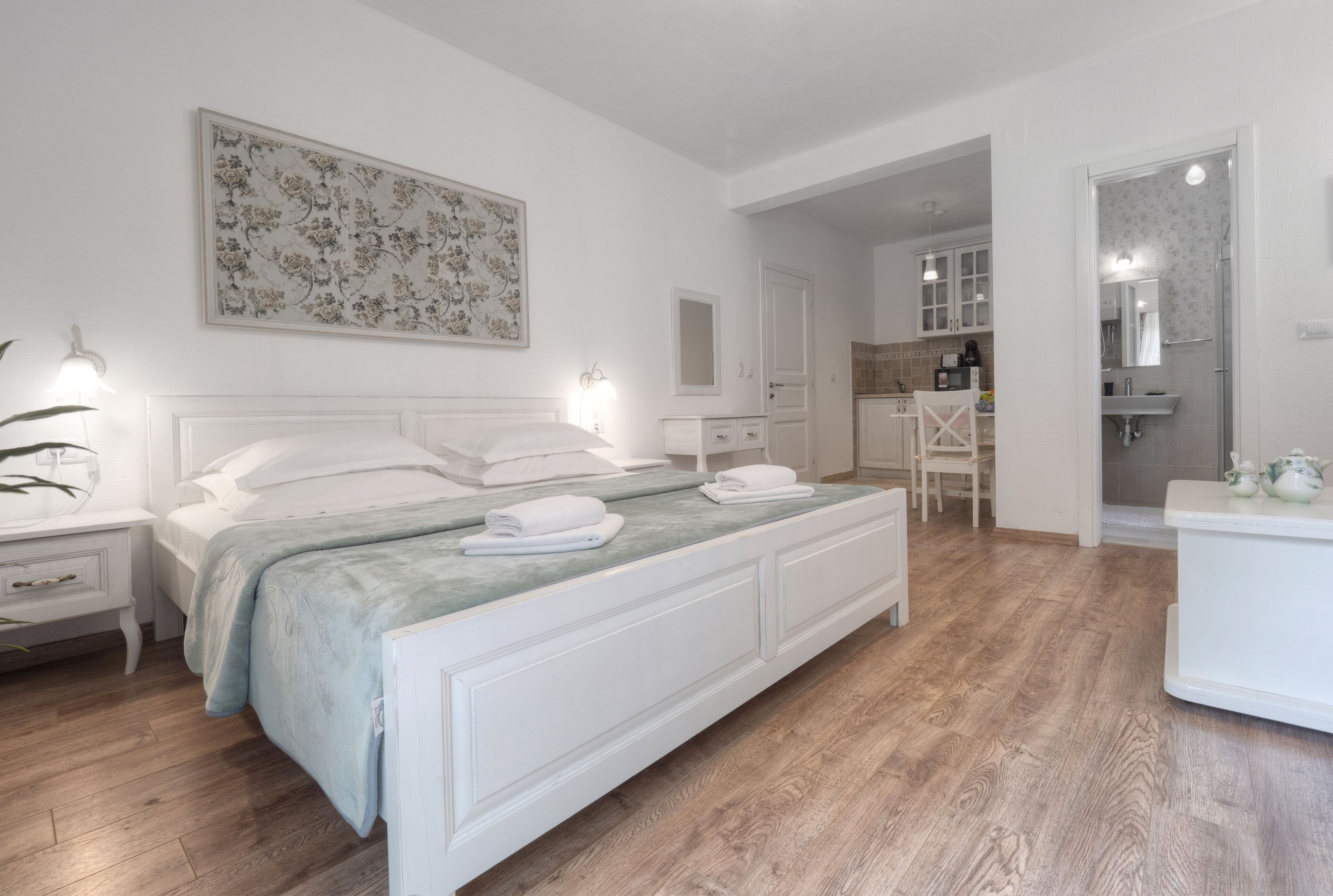 Een slaapkamer met een bed, nachtkastjes, een dressoir en een zichtbare badkamer door een open deur.