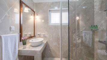 Un baño moderno con un espejo grande, un lavamanos redondo, una cabina de ducha de vidrio y una ventana pequeña.