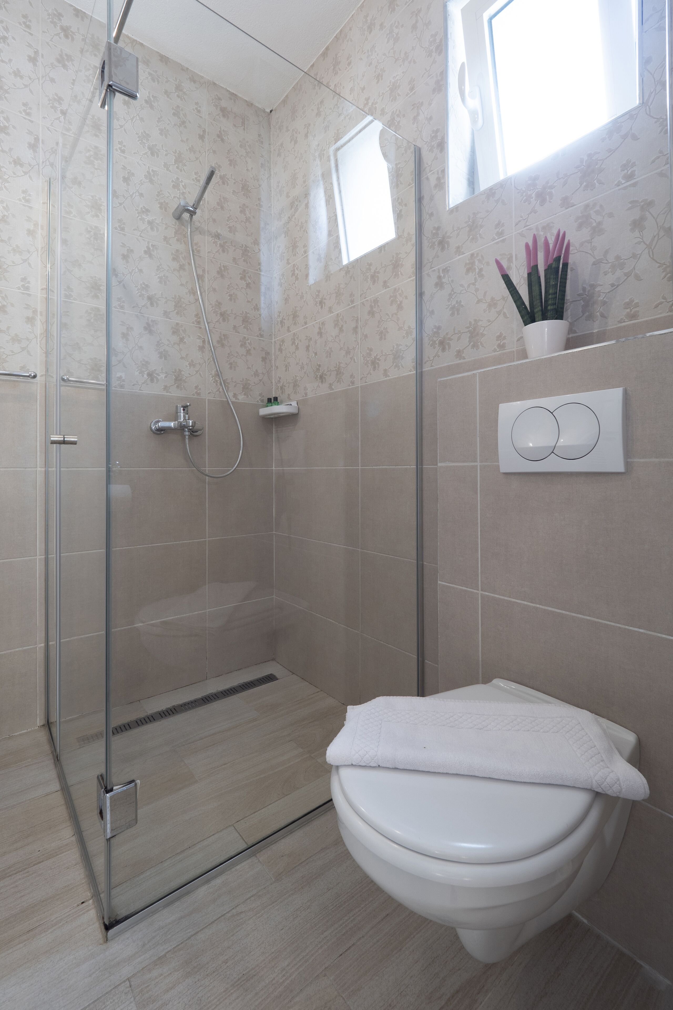 Een badkamer met een douchecabine van glas, een toilet en een wandbediening voor de spoeling.