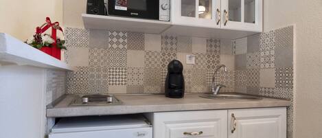 Una cocina compacta con gabinetes blancos, microondas, cafetera y pileta.