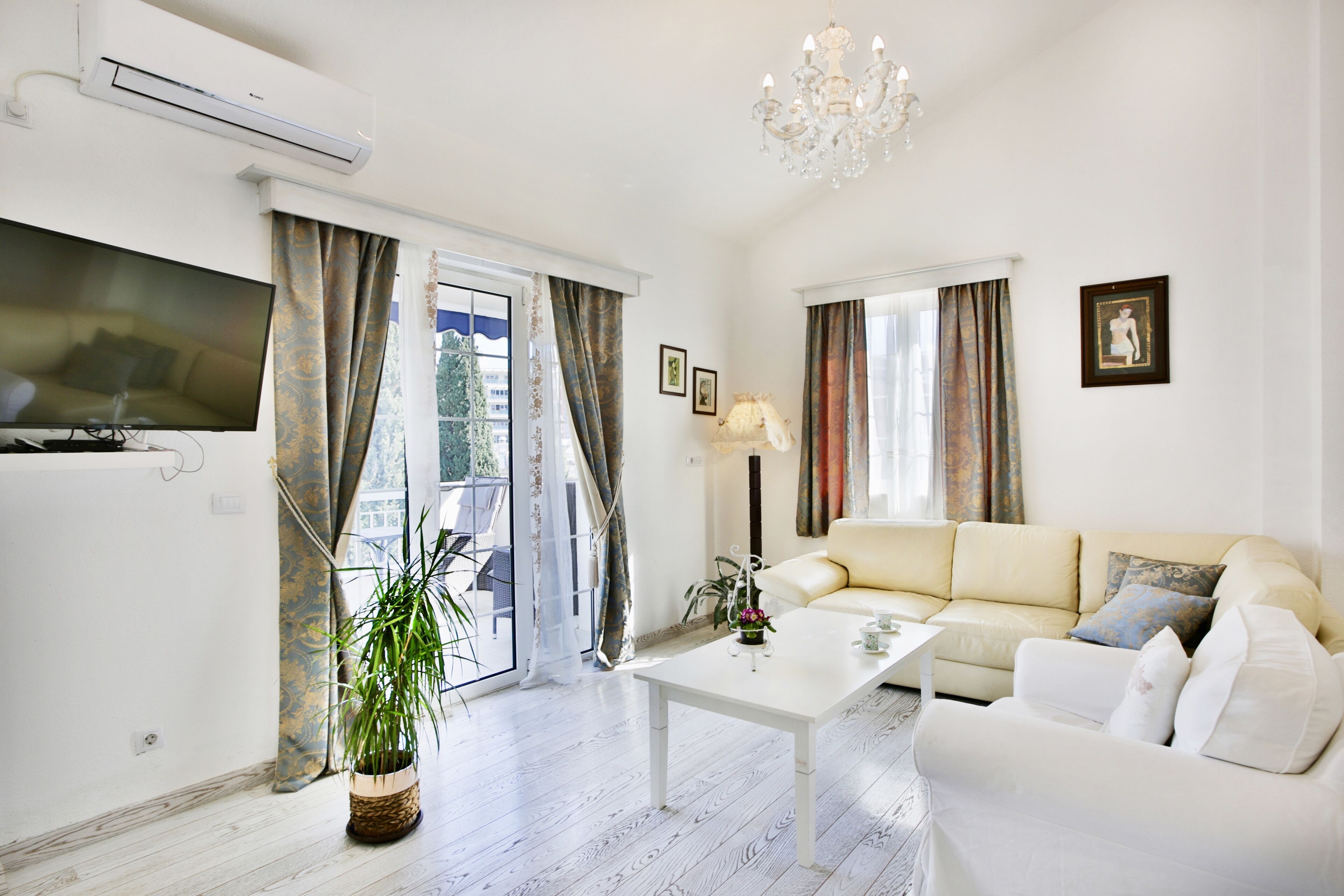 Ein modernes Wohnzimmer mit einem weißen Sofa, einem Couchtisch und einem Fernseher. Eine Topfpflanze und eine Deckenleuchte sind ebenfalls vorhanden.