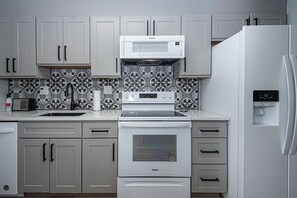 A kitchen with grey cabinets, a white microwave, a stove, and a refrigerator.
