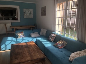 A living room with a blue sofa, a wooden coffee table, and a window with curtains. - The waterfall balcony (Trans-en-Provence)
