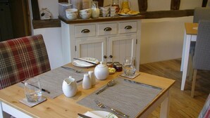 Una mesa de comedor dispuesta con platos, cubiertos y copas, junto a una silla de madera y un cojín de cuadros.