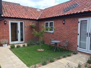 A brick house with a tiled roof, a small lawn, and a patio with two chairs. - Grove Barn Bed and Breakfast (Harleston)