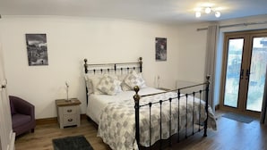 Un dormitorio con una cama, mesitas de noche, un sillón morado, una ventana con persianas y una puerta.