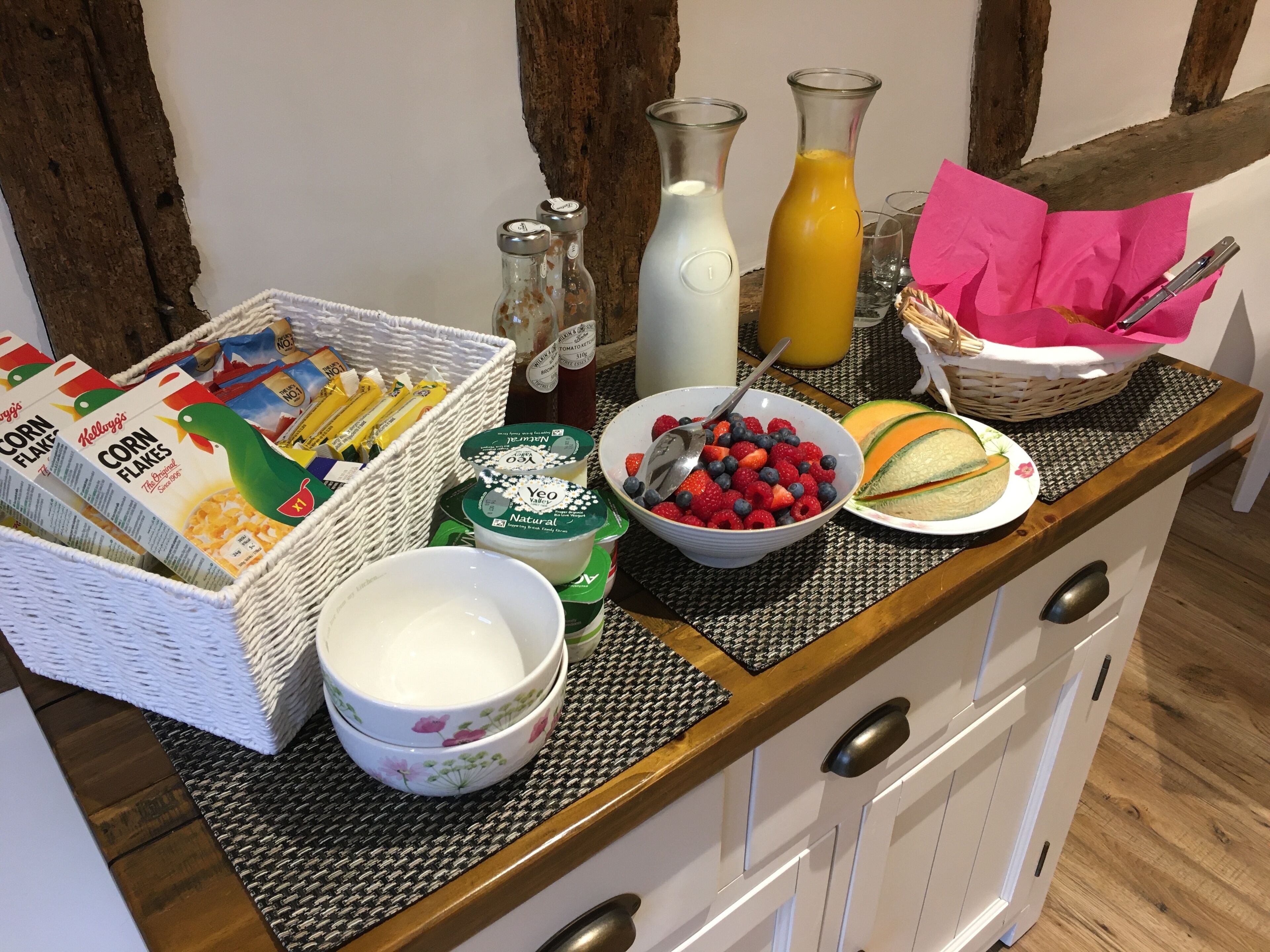 En morgenmadsbuffet med cornflakes, yoghurt, frisk frugt og drikkevarer på et træbord.