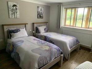 A bedroom with two beds, a window with blinds, and two wall-mounted pictures. - Grove Barn Bed and Breakfast (Harleston)