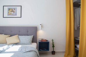 Un dormitorio con cama, una mesita de noche con lámpara, un cuadro enmarcado en la pared y una planta en maceta.