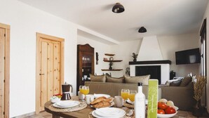 Comedor con mesa de madera dispuesta para el desayuno, con cruasanes, jugo y una botella de agua.