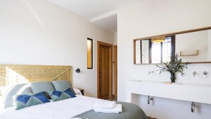 Habitación de hotel con cama, mesita de noche, espejo y baño con lavamanos y ducha.