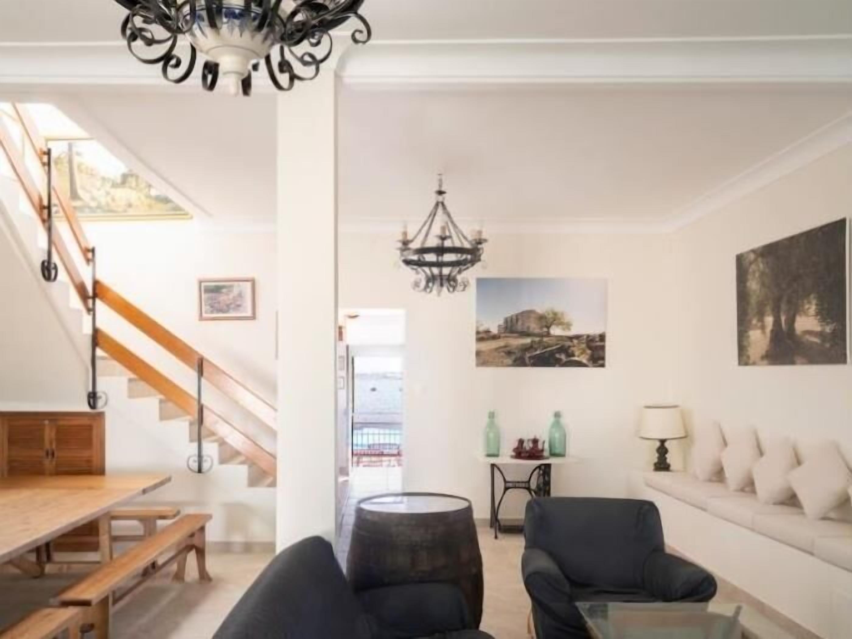 A spacious living room with a wooden staircase, a chandelier, a sofa, and a dining table.