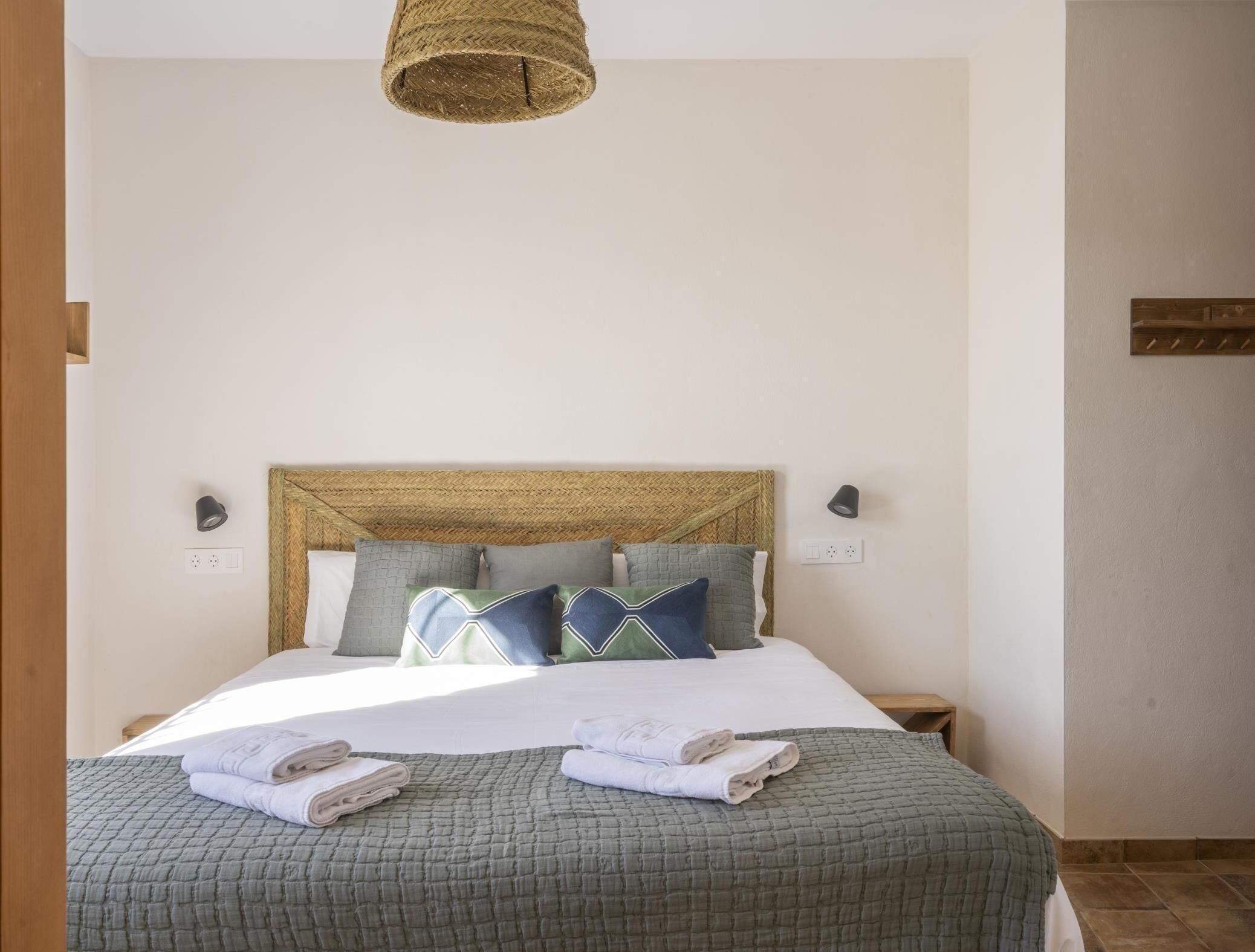 A neatly made bed with a green quilt, two pillows, and two folded towels.