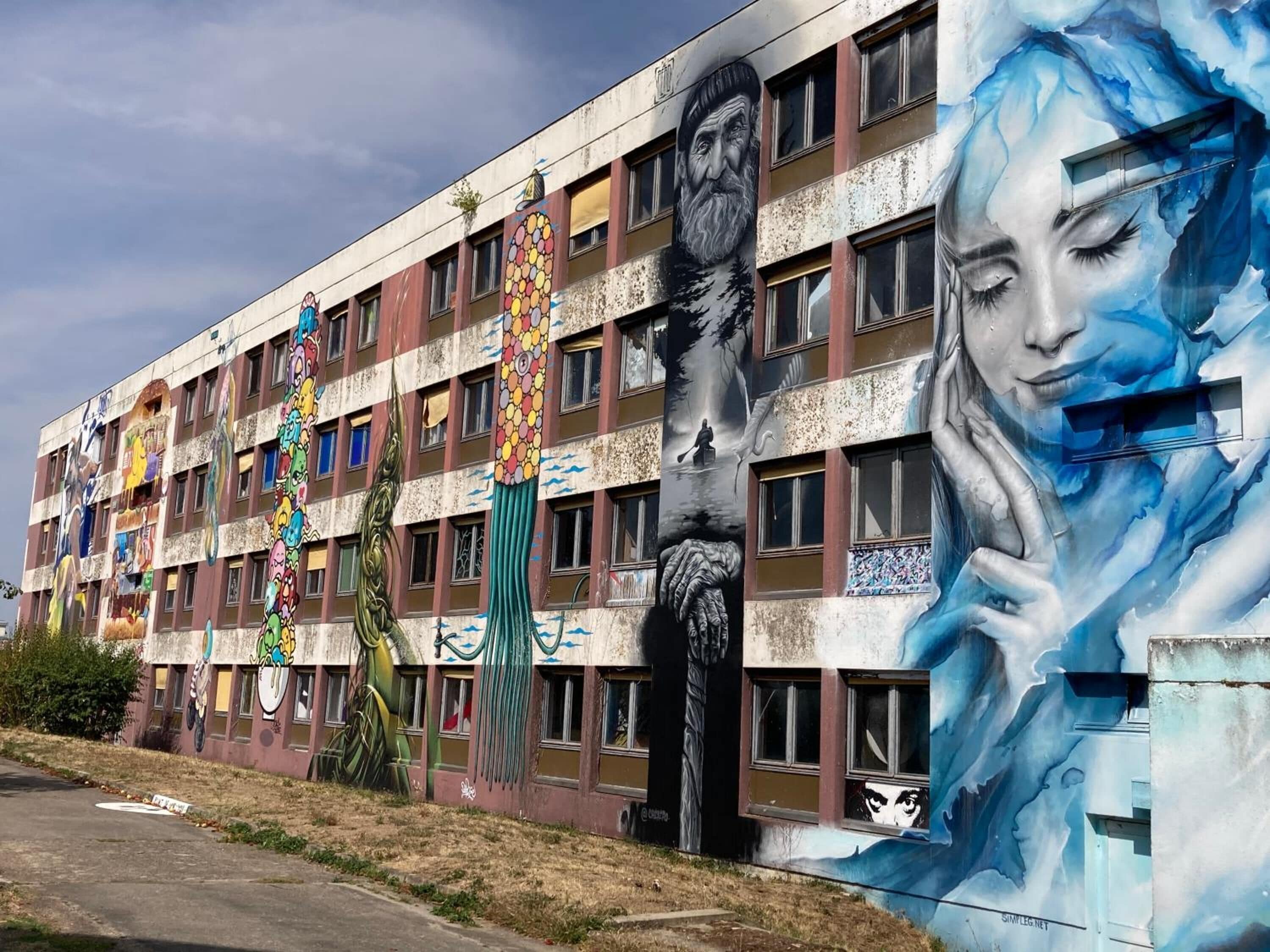 A building with a large mural on its facade, featuring various artistic elements and figures.