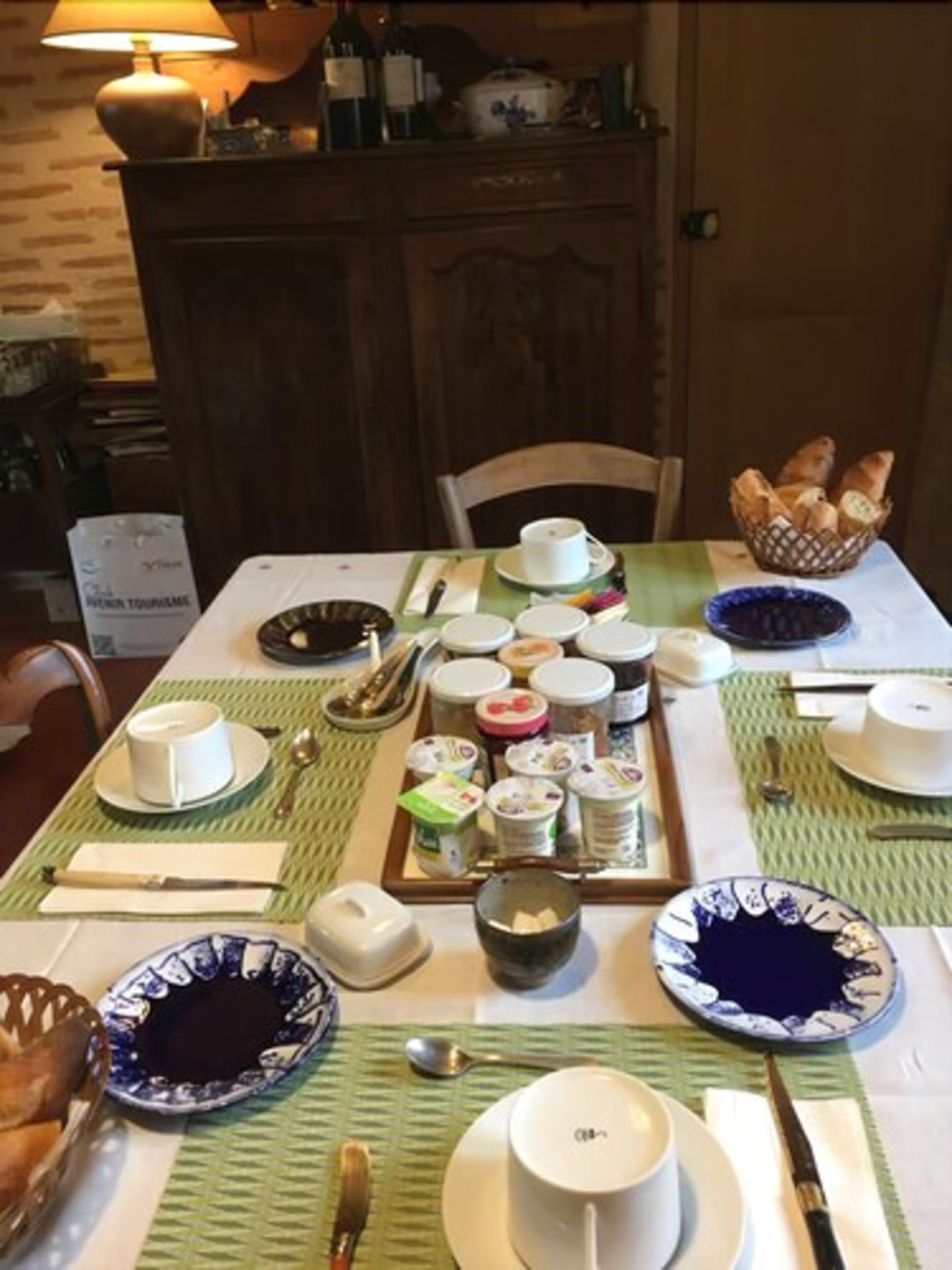 A dining table set with various dishes, including bowls, plates, and utensils, in a room with wooden furniture and a lamp.
