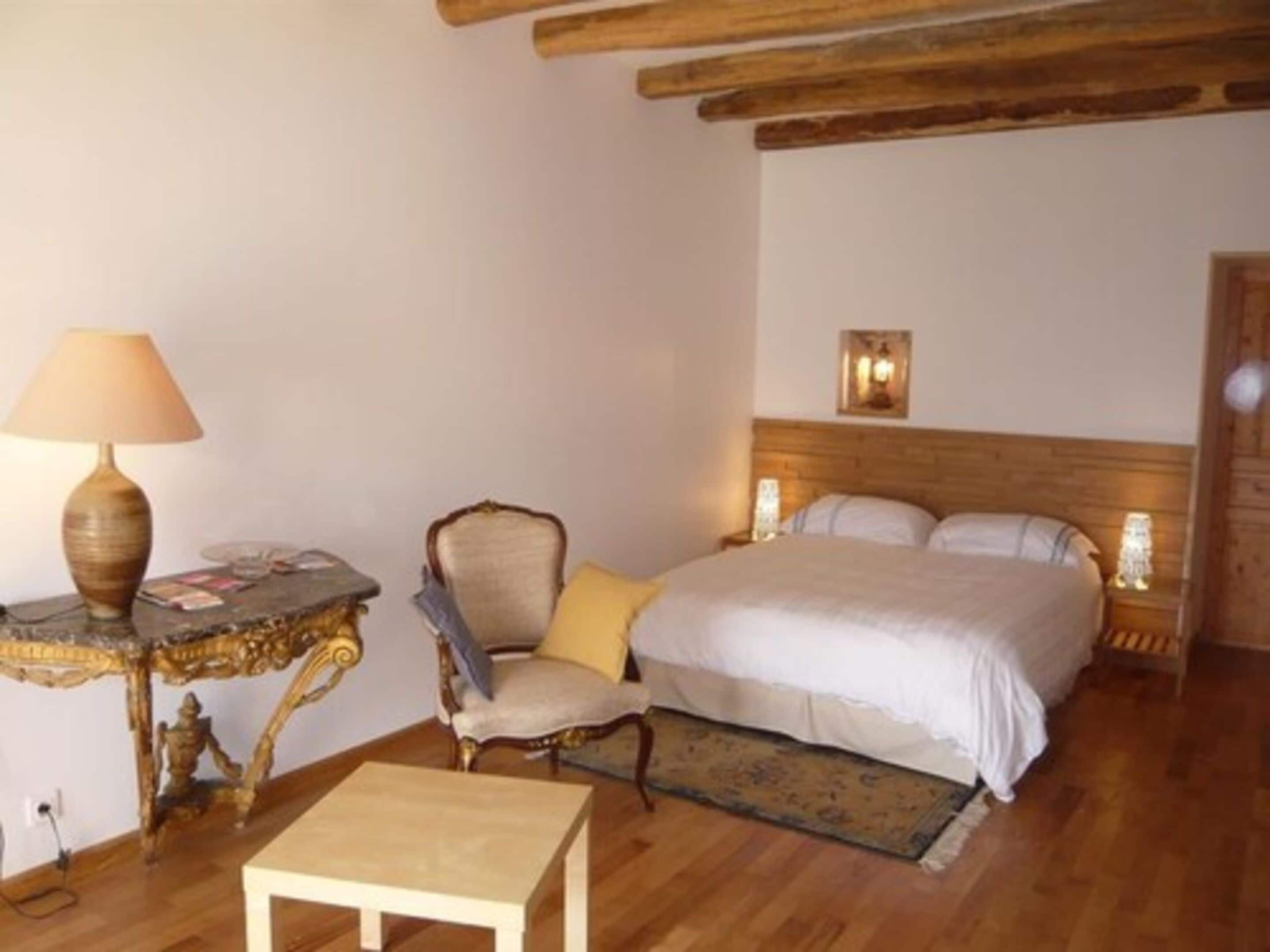 A bedroom with a bed, a chair, a small table, and a lamp.