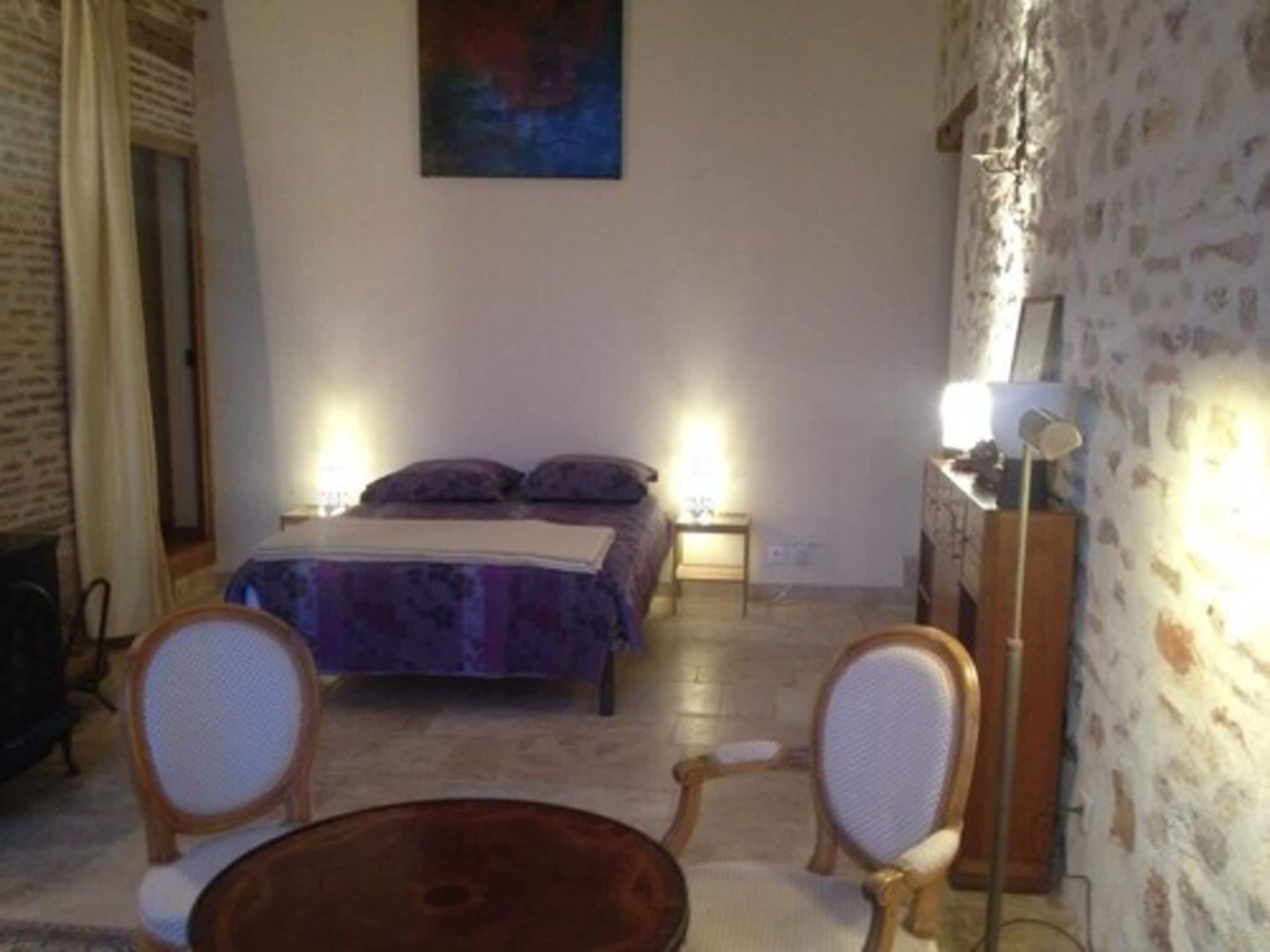Une petite pièce confortable, avec un lit, deux chaises, une table et un tableau accroché au mur.