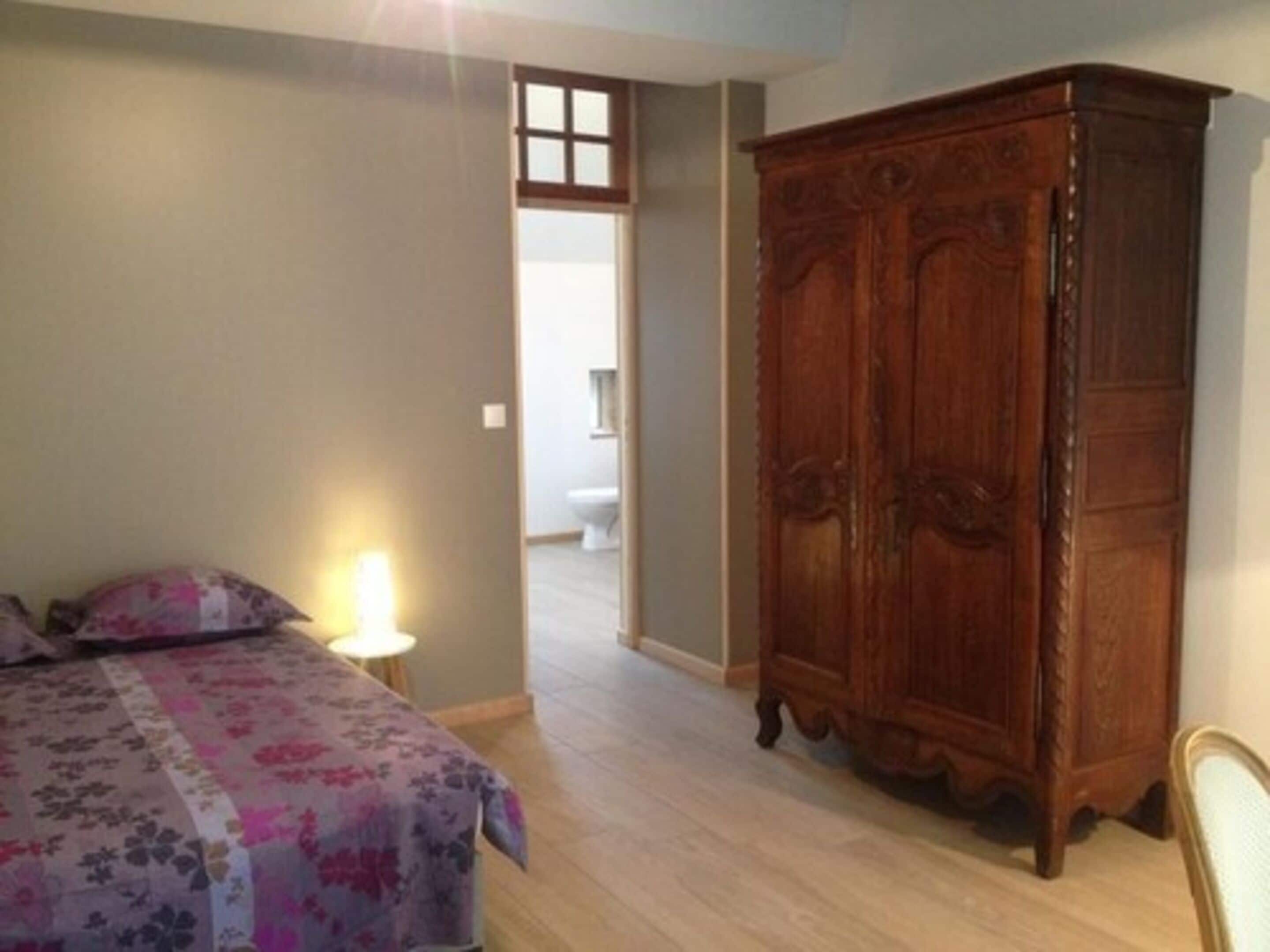 Een slaapkamer met een houten garderobe, een bed met een bloemenprint en een nachtkastje met een lamp.