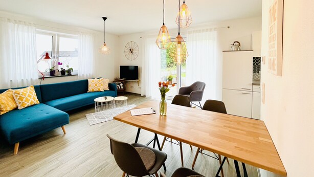 Ein modernes Wohnzimmer mit einem blauen Sofa, einem Holzespeisetisch und Pendelleuchten.