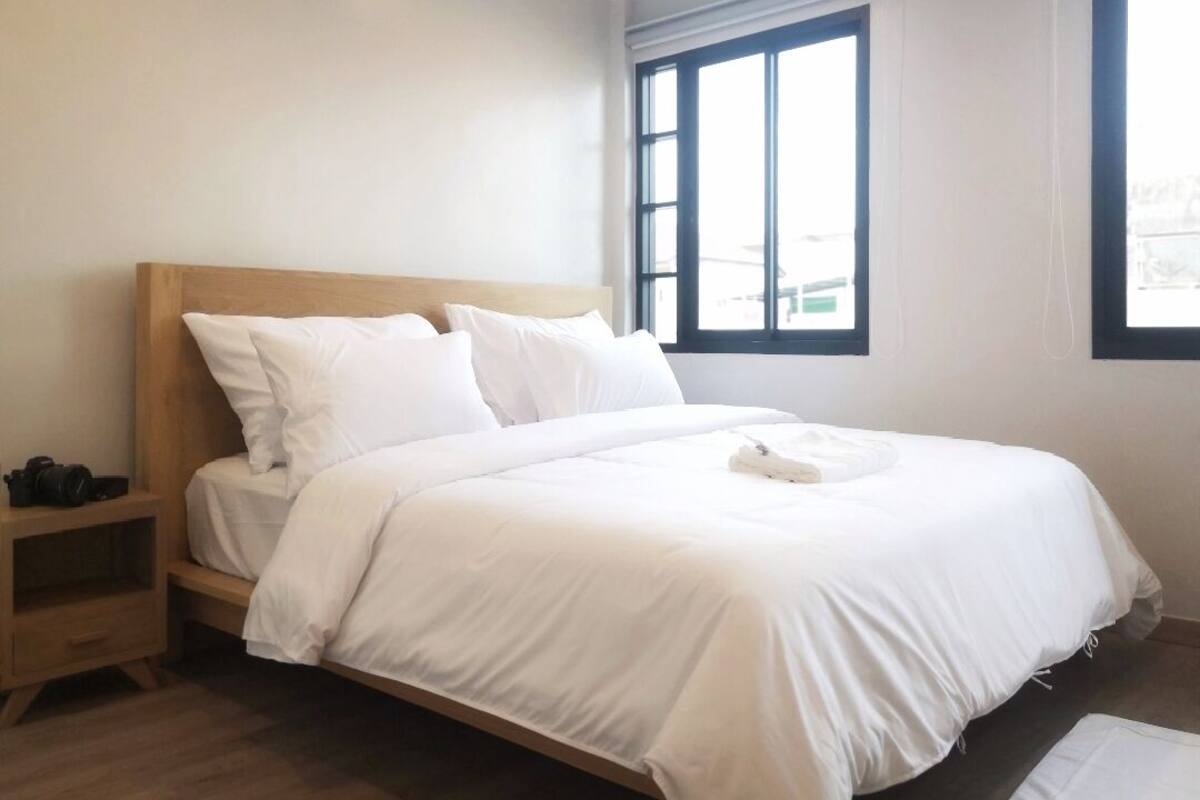 A neatly made bed with white bedding in a room with a wooden headboard and a small wooden nightstand.