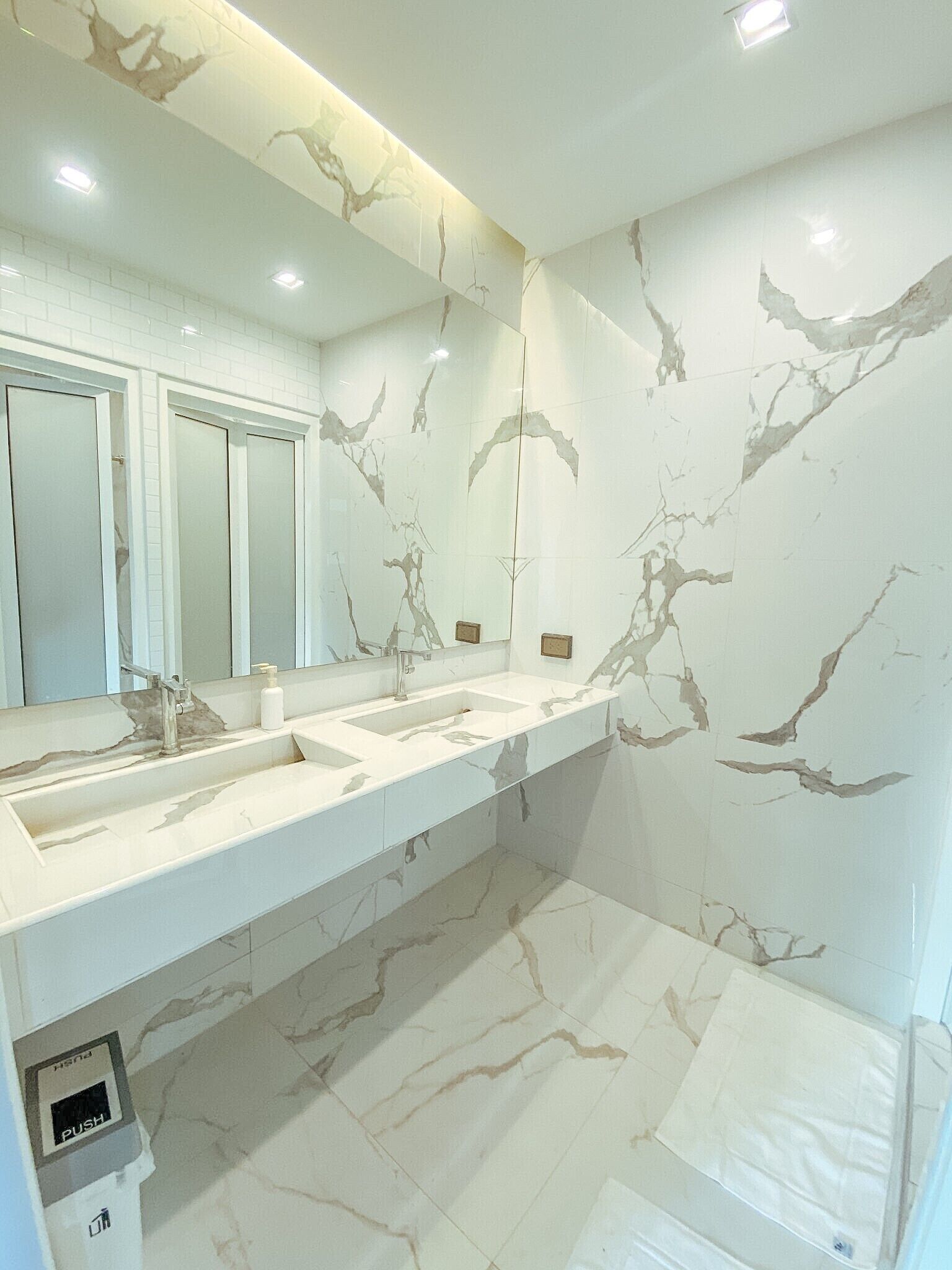 A modern bathroom with marble walls and a large mirror. There are three sinks and a toilet.