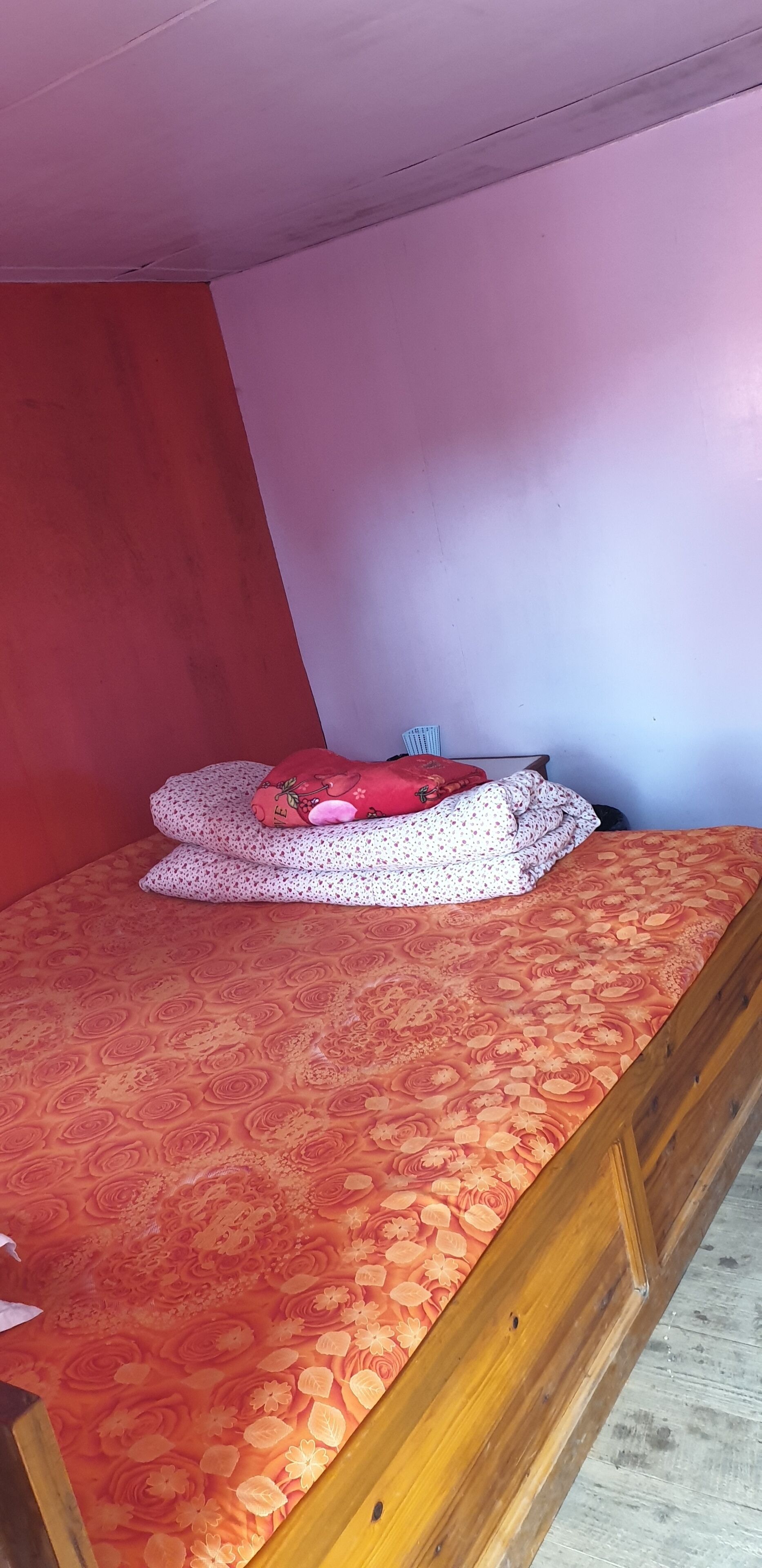 Una cama con colcha naranja estampada con motivos florales, un almohadón rojo y un almohadón blanco con diseño floral.