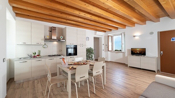 A modern kitchen with white cabinets, a dining area with a wooden table and chairs, and a living area with a television.