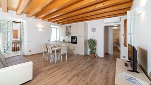 A modern kitchen with wooden beams, a dining area with a table and chairs, and a living room with a sofa and a TV.