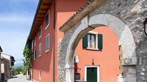 A narrow street with a red building featuring a stone archway, a green door, and shutters.