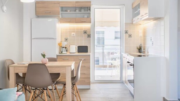 Eine moderne Küche mit Holzschränken, einem Essbereich mit Tisch und Stühlen sowie Blick auf den Balkon.