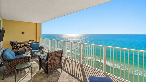 A balcony with wicker furniture, a TV, and a view of the ocean. - 4 Free Beach Chairs & 2 Umbrellas, Updated Beach-Front Condo, Large Balcony! (Panama City Beach)