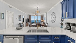 A modern kitchen with a central island, a built-in dishwasher, and a dining area with a view. - 4 Free Beach Chairs & 2 Umbrellas, Updated Beach-Front Condo, Large Balcony! (Panama City Beach)