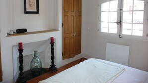 Una camera da letto con un letto, una porta in legno, una finestra, un camino e uno scaffale con un quadro incorniciato.