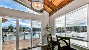 A room with large windows overlooking a marina, a wooden deck, and a dining area with chairs and a table.
