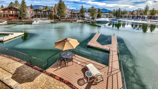 A waterfront property with a dock, a lounge area with a table and chairs, and a view of the surrounding buildings and mountains.