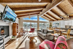 A spacious living area with a fireplace, a large sofa, a dining table, and a kitchen area.
