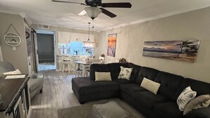 A modern living room with a sectional sofa, a dining area, and a kitchen in the background. - Beach Vacation Condo (Myrtle Beach)