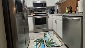 A modern kitchen with stainless steel appliances, white cabinetry, and a wooden floor. - Beach Vacation Condo (Myrtle Beach)