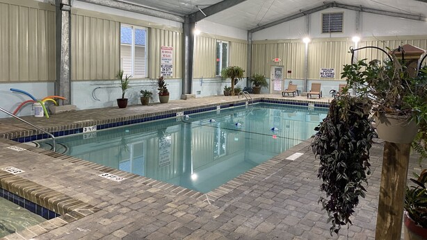 An indoor swimming pool with tiled edges, potted plants, and safety signs. - Beach Vacation Condo (Myrtle Beach)