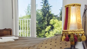 A bed with a patterned pillow, a bedside lamp with tassels, and a view of greenery through a window. - Lovely spacious house close to parks and tramway (Antwerpen)