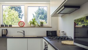 A modern kitchen with white cabinets, a black countertop, a gas stove, and a window with a view of trees. - Lovely spacious house close to parks and tramway (Antwerpen)