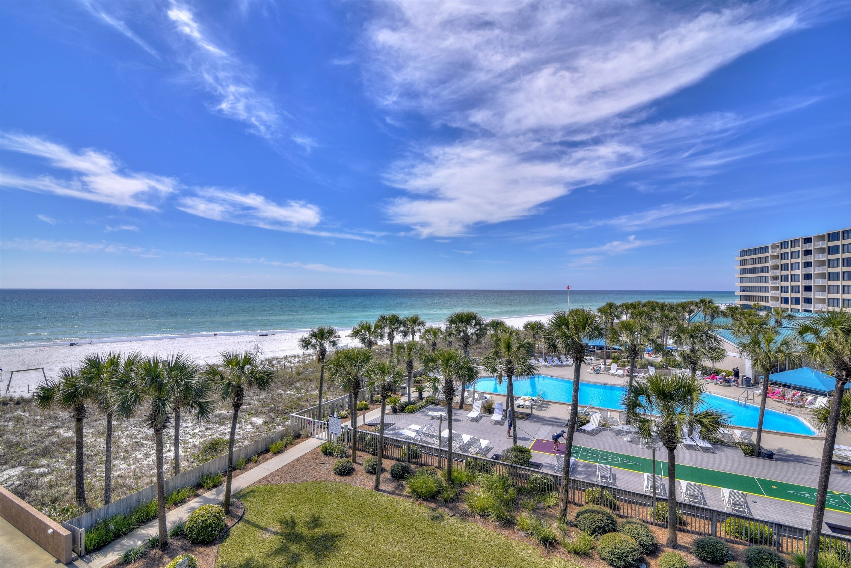 Vista de una playa con piscina, palmeras y un edificio de hotel.