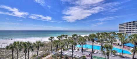 Vista de una playa con piscina, palmeras y un edificio de hotel.