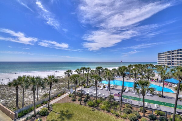 Blick auf einen Strand mit Pool, Palmen und einem Hotelgebäude.