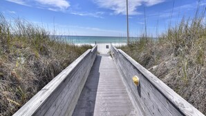 Een houten looppad dat naar een strand leidt, onder heldere luchten.