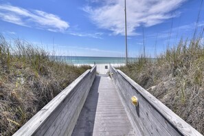 Ein hölzerner Steg führt zu einem Strand bei strahlend blauem Himmel.